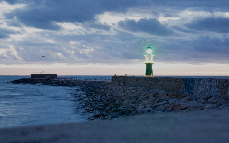 Wolkiger Abendhimmel zur "Blauen Stunde" über der Warnow-Mündung und der Ostsee bei Warnemünde, im Hintergrund das grüne Warnemünder Molenfeuer