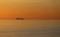 A summer sunrise over a calm Baltic Sea with the silhouette of a ship on the horizon colours the water and the sky deeply red.