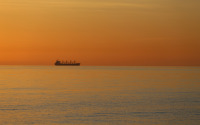 A summer sunrise over a calm Baltic Sea with the silhouette of a ship on the horizon colours the water and the sky deeply red.